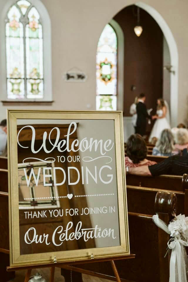 welcome sign at Devotions Wedding Chapel with wedding ceremony in background