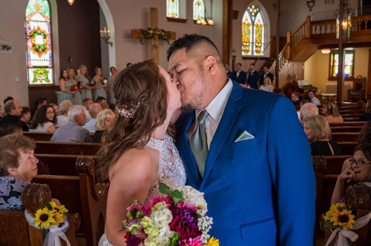 Interior Green Bay wedding photo with bride and groom kissing in the foreground with guests in the background